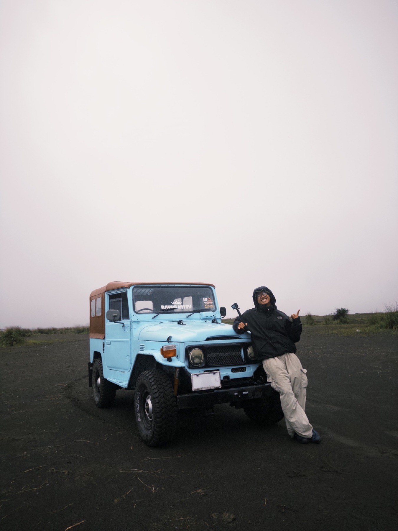Aqmal Nizam leaning on a pale blue jeep on an open hilltop